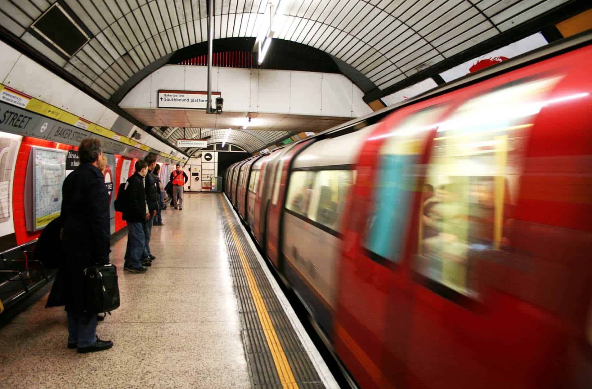 People stand waiting at Baker Street tube station while a tube rushes past