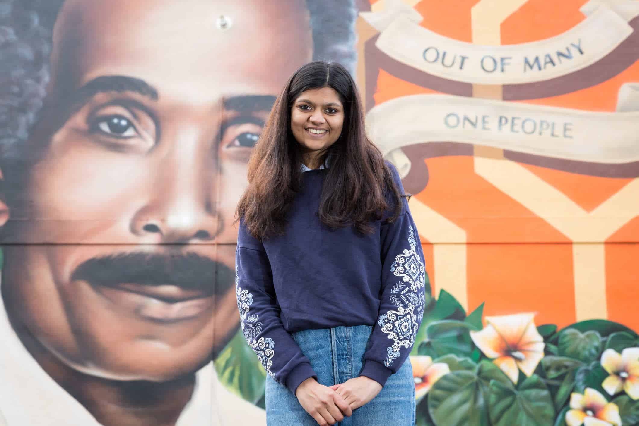 Paridhhi stands in front of a large mural, smiling at the camera.