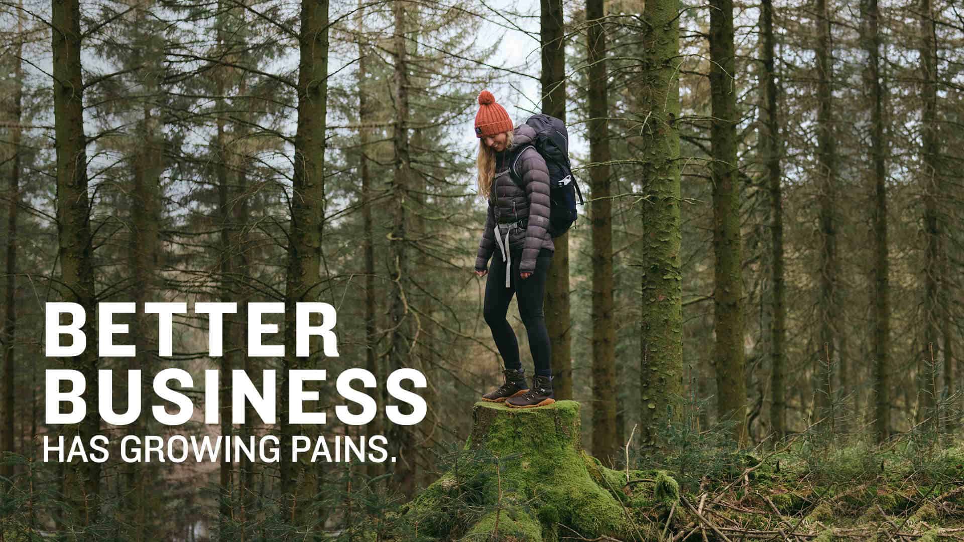 Person stood on a mossy tree stump in a wood. They're wearing Vivobarefoot shoes, a bobble hat and a rucksack. Text reads "Better business has growing pains."